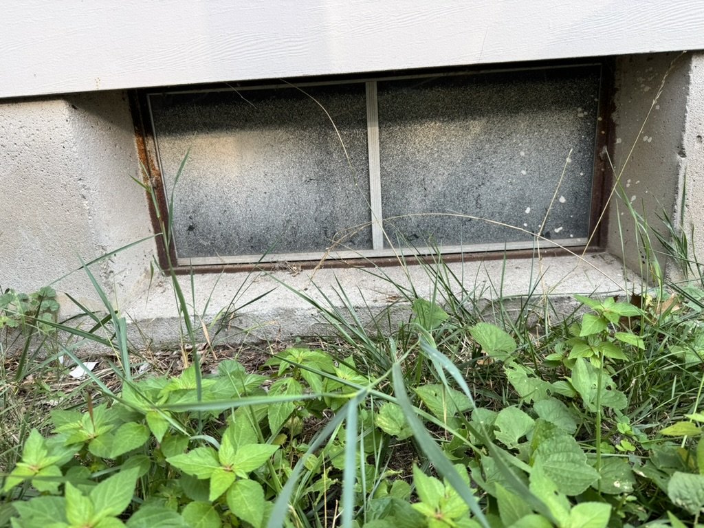 Old rusted basement window with grimy glass before replacement, West Michigan